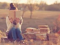 reading teen girl in field of grass with books next to her